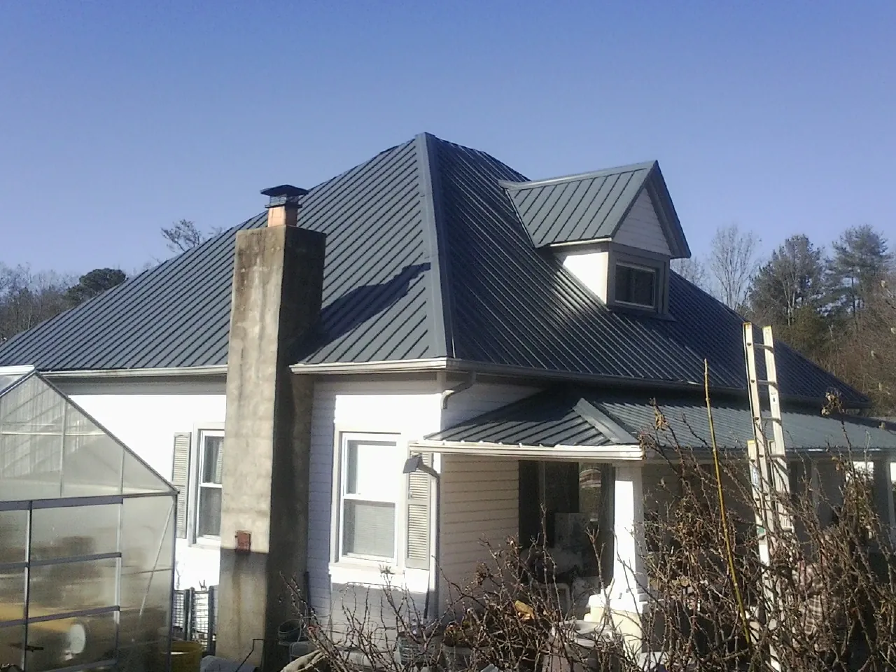 Dark blue standing seam metal roof on a white farmhouse with dormer — Slate & Tile Roof Repair by Roofing Brothers in Lannon