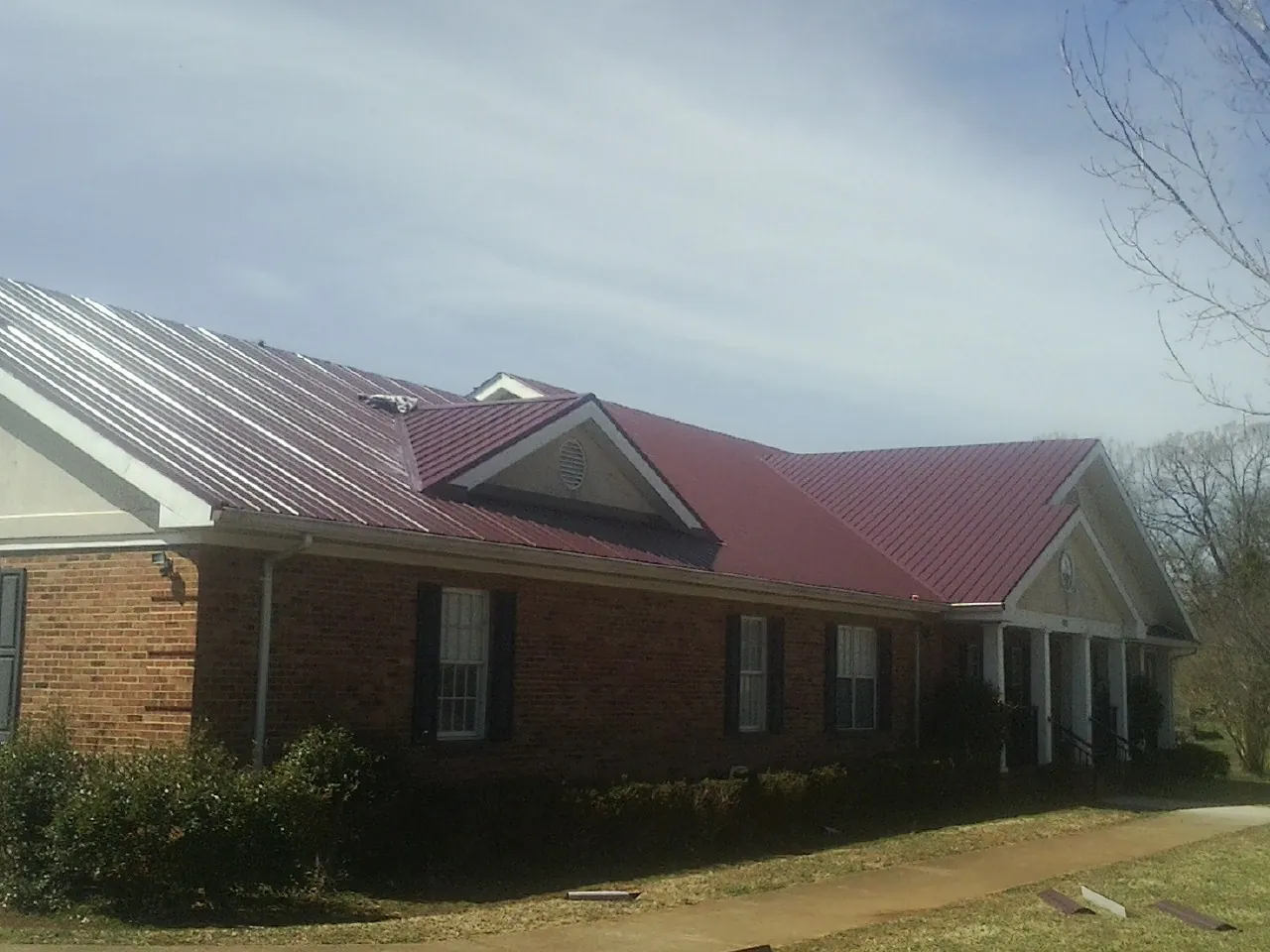 Red metal roof with gabled entries on a long brick building, from a Hail Damage Roof Repair job in Lannon