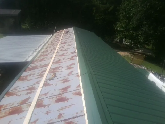 Old rusted panels beside newly installed green metal roofing — Wind Damage Roof Repair by Roofing Brothers in Lannon