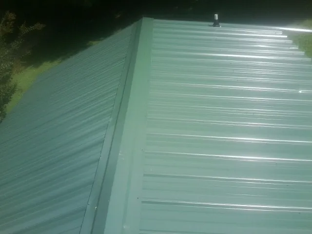 New green metal panels meeting at the ridge of a roof — Flat Roof Repair work by our crew in Lannon