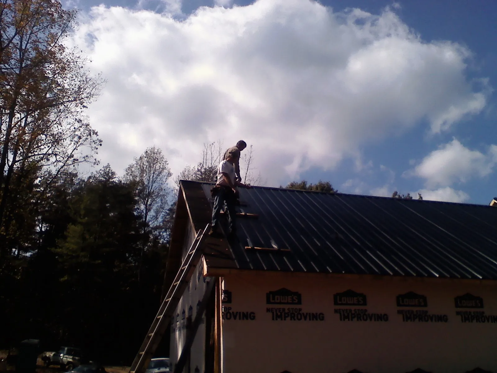 Roofer fastening dark metal panels high against a cloudy sky, from a Roof Inspection job in Lannon