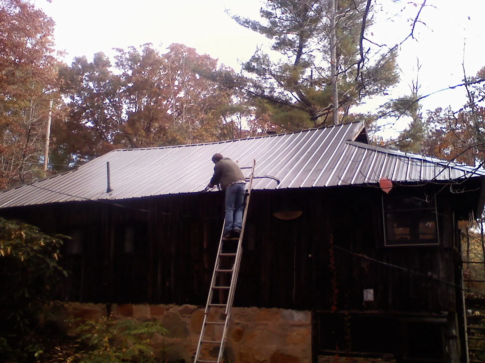 Roofer on a ladder working along the edge of a cabin metal roof in Lannon