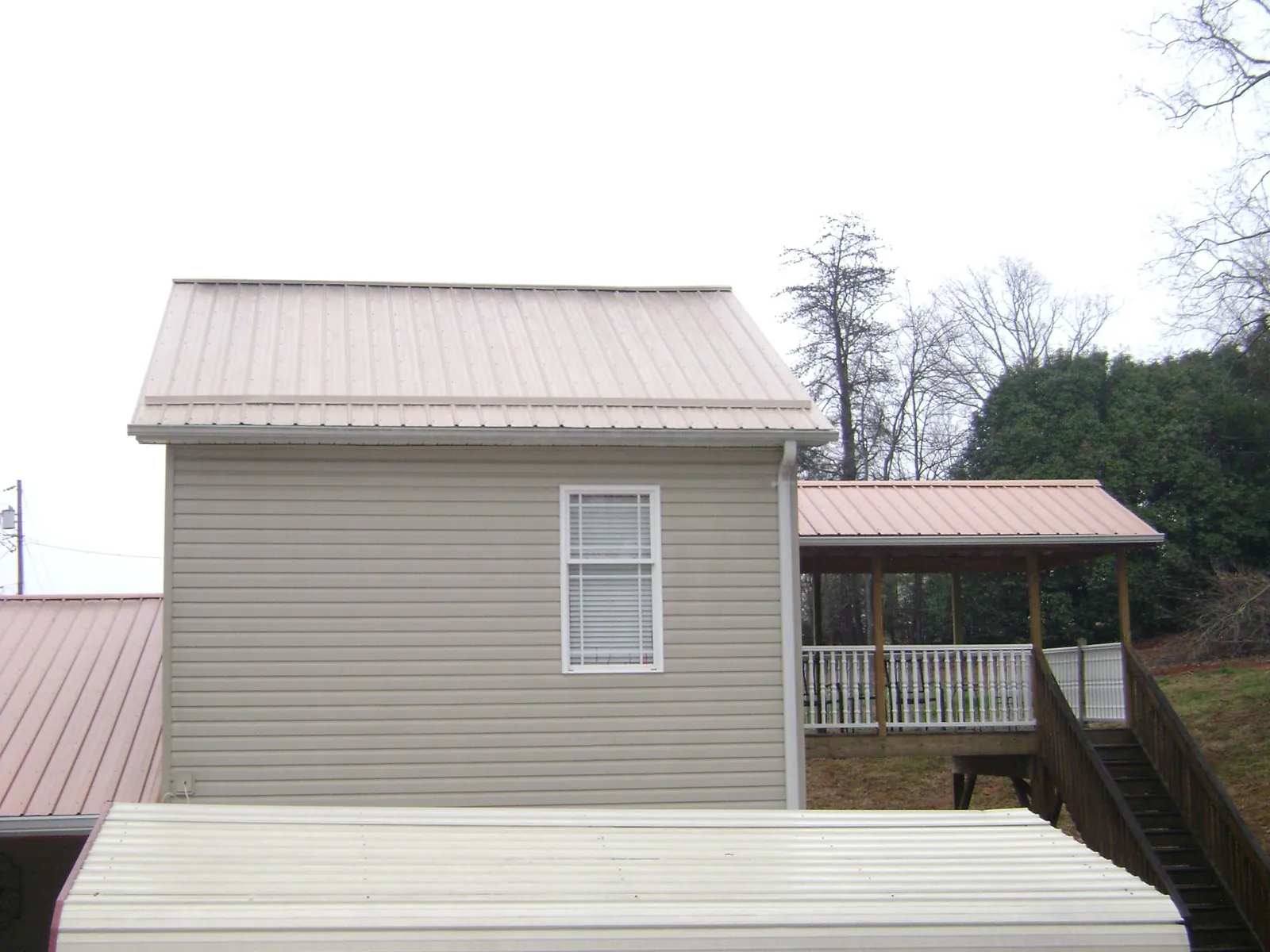 Tan metal roofs on a two story addition and attached porch, from a Roof Replacement job in Lannon